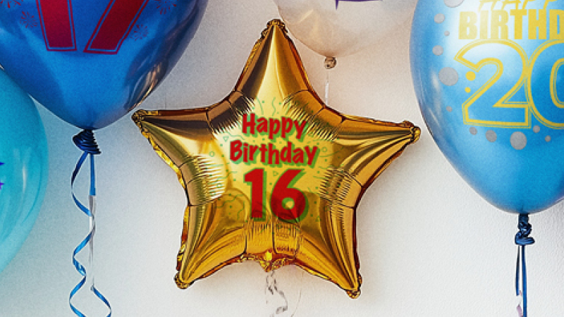A cluster of colourful balloons featuring different birthday year numbers are displayed on them. The most prominent ballon in the middle is shaped like a gold star with the words “Happy Birthday 16” printed on it. 