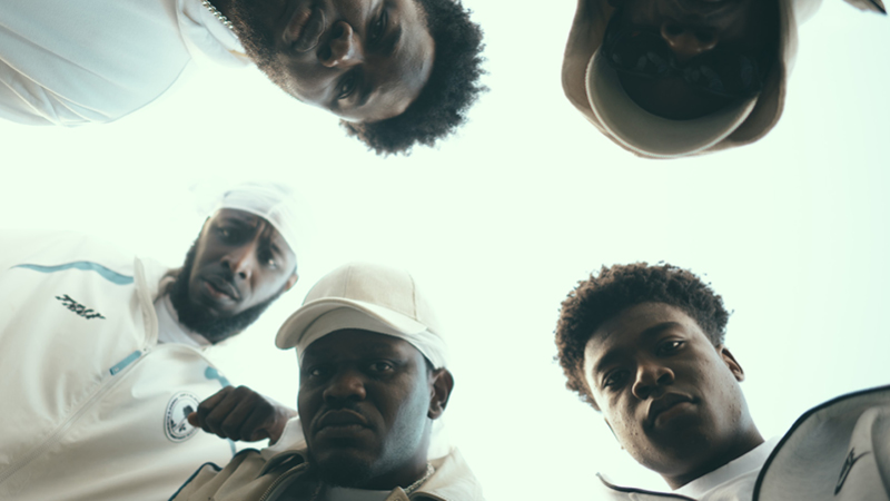 Five people in casual clothing are looking down at the camera with a sky background.